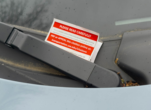 red parking citation beneath windshield wiper of a car