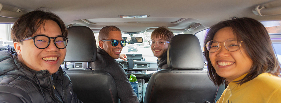 four happy students in a car carpooling together