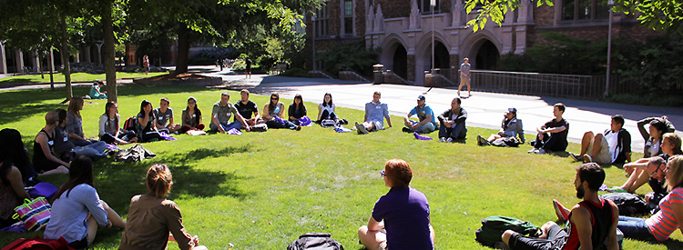 students at class seated in a circle on lawn