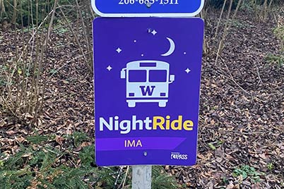 purple sign with white and yellow text for night ride indicating ima stop 