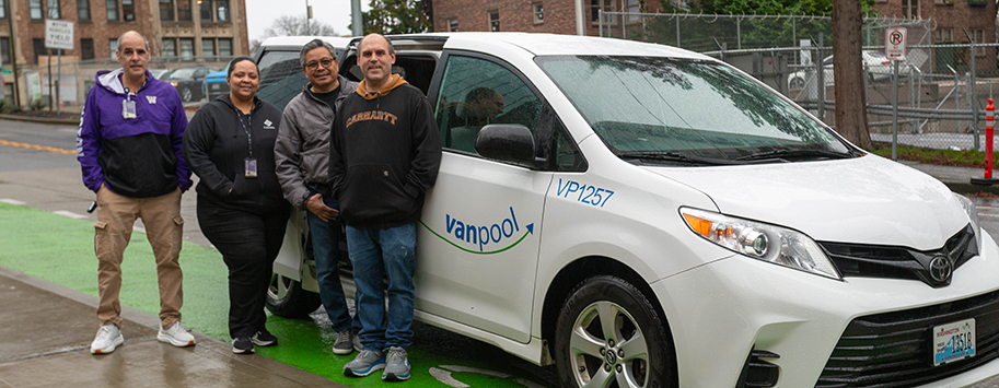 Four smiling employees standing to the car they vanpool in