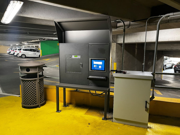 a closed key manager locker with screen display, keyboard and mouse roller ball inside a parking garage with ucar vehicles in background