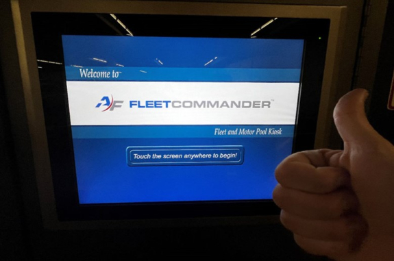 key manager kiosk screen showing welcome screen and touch the screen anywhere to begin message with person's hand in foreground with a thumbs up