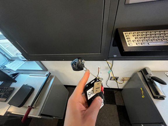 metal key, key card and car key fob in person's hand in front of key manager kiosk