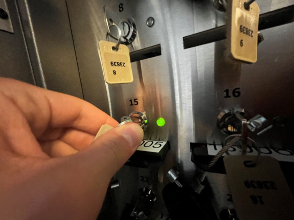 person's hand holding metal key inserted into key hole in key manager box at position 15 with green light illuminated