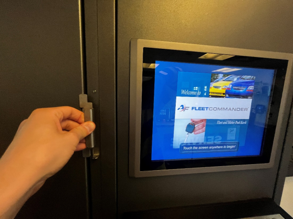 person's hand holding door handle to key manager box in closed position with touch screen display to the right