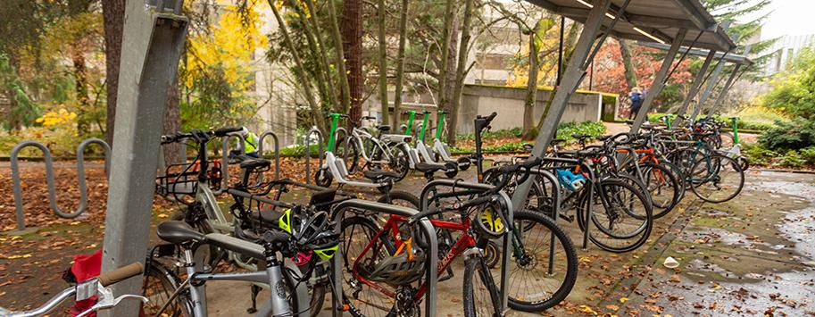 many bicycles and scooters parked around a partially covered bike parking area