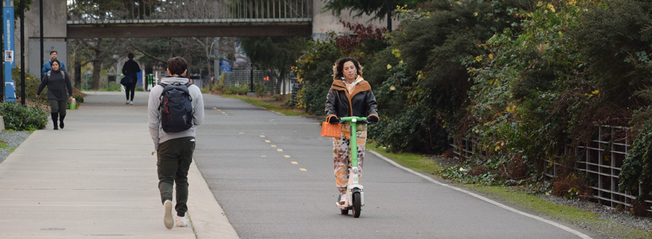 woman riding a green and white electric scooter on burke-gilman trail