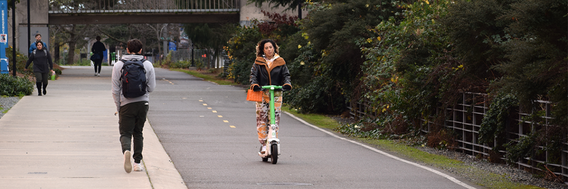 A woman rides on a green and white scooter on a bike trail
