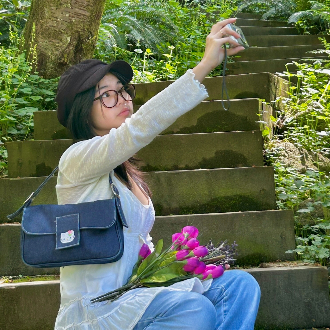 A photo of Kayla sitting on stairs outside taking a selfie with a digital camera