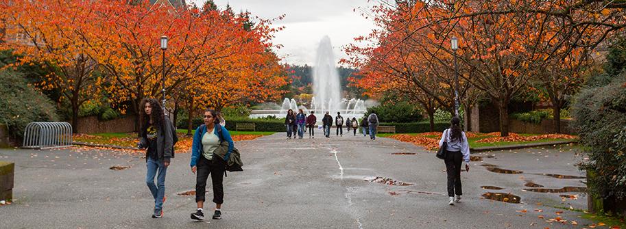 students walking to class with Drumheller Fountain and trees with autumn colored leaves in the background